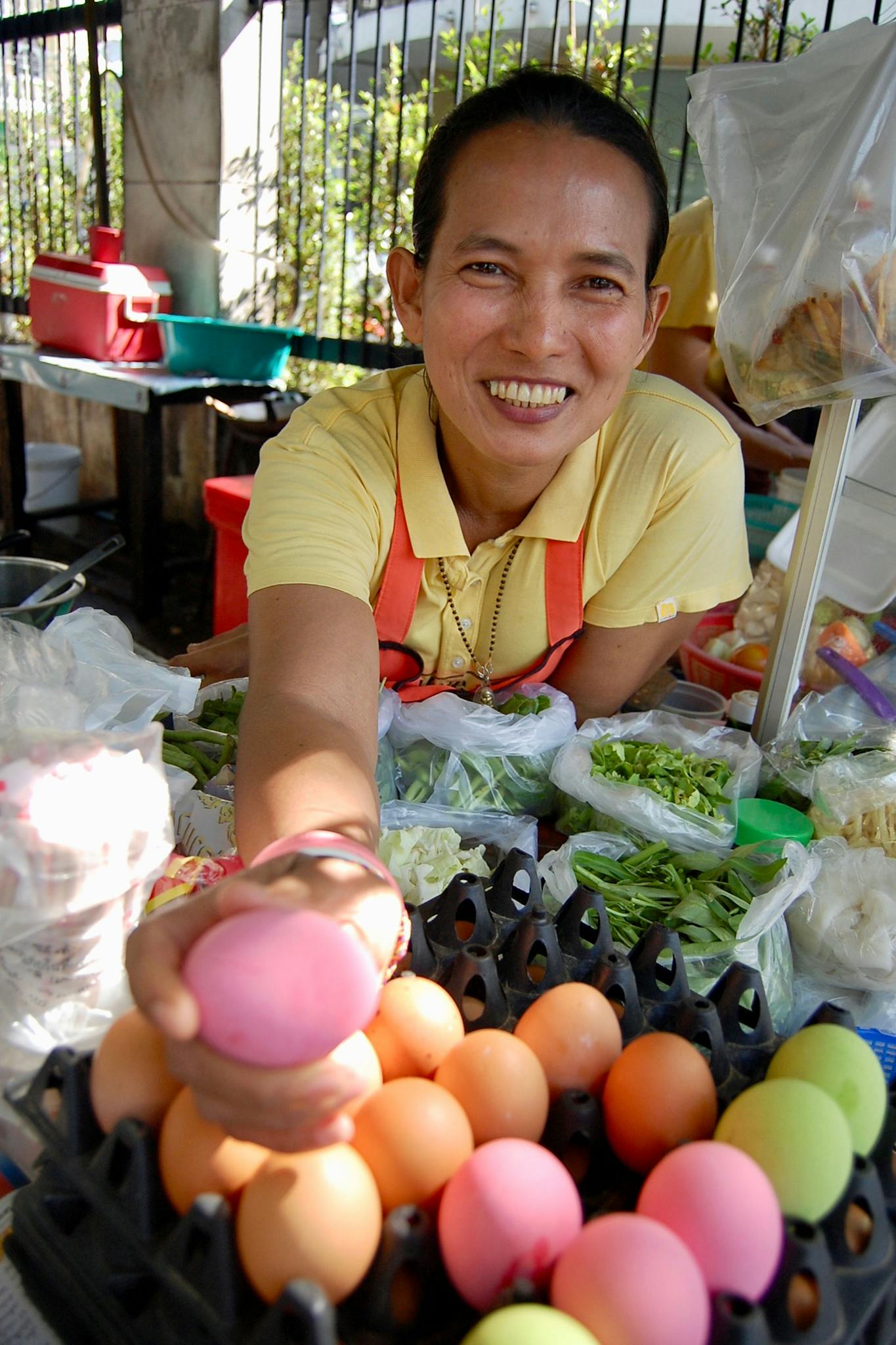 Friendly vendor at outdoor market offers colorful eggs with a warm smile.